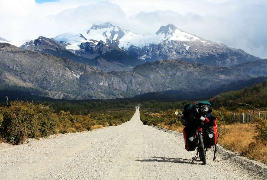 A Lightweight Bike Touring Gear List A bike packed with supplies stopped on a gravel road leading to snowy mountains