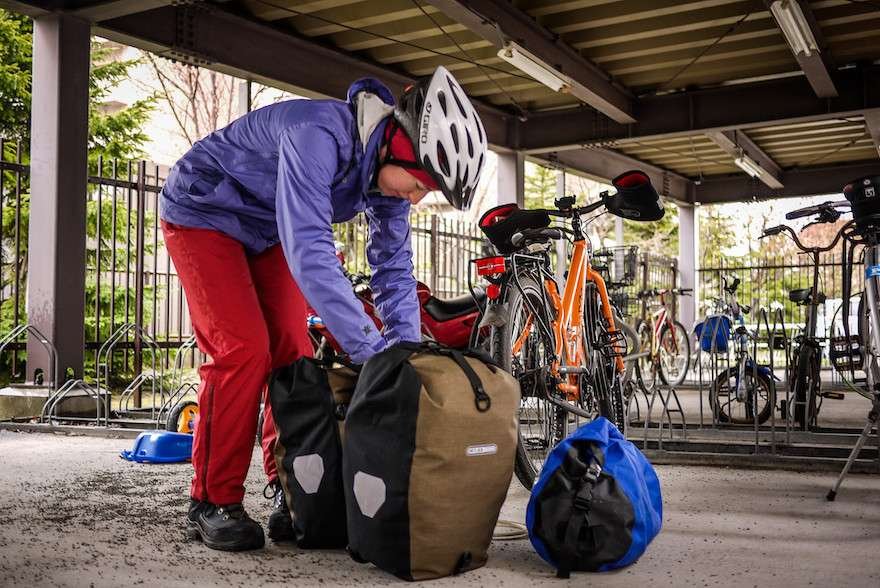 A Lightweight Bike Touring Gear List A cyclist digging into her pannier bags after parking her bike
