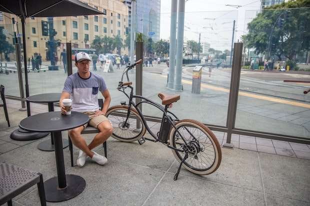 Man sitting at a coffee shop drinking coffee next to his bike