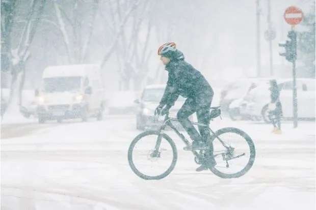 Cyclist riding bike in a blizzard after learning how long bicycle brake pads last